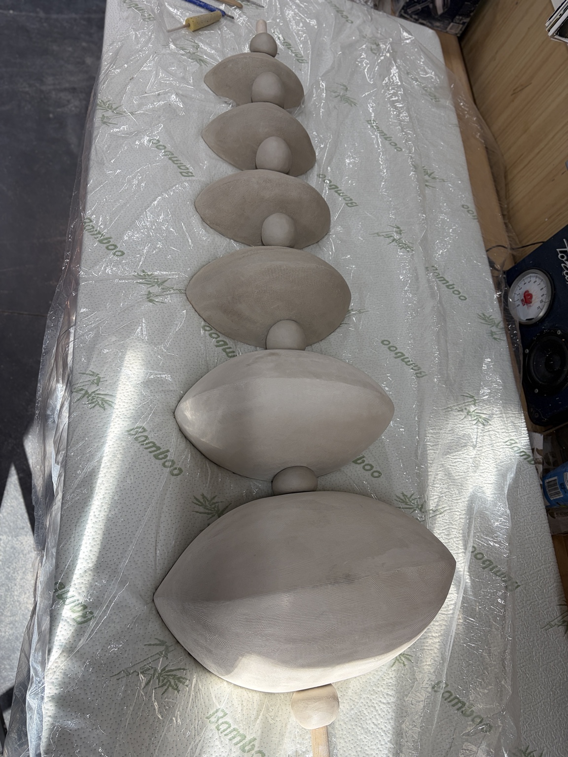 Unfired pale ceramic pod forms and spherical spacers arranged in sequence